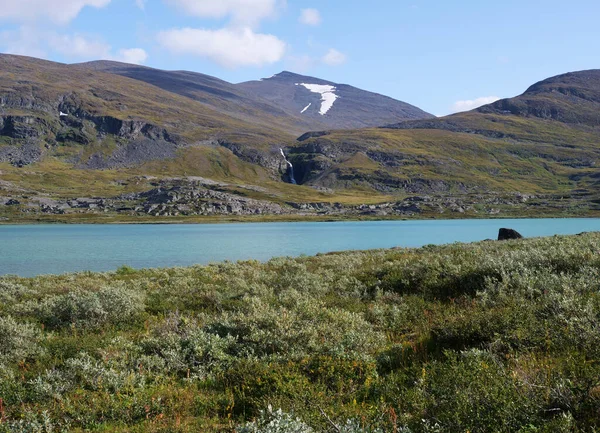 Lappföldi természet táj kék gleccser tó Allesjok közelében Alesjaure, nyírfa erdő, hó sapkás hegyek és vízesés. Észak-Svédországban, a Kungsleden túraútvonalon. Nyári napsütéses nap — Stock Fotó