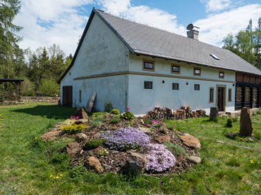Bahçeli eski ahşap bir ev, pembe Phlox, Armeria maritima, deniz taşları, Bergenia veya fil kulakları, karanfil rengi çiçek ve çardak pergola ile dolu bir kaya bahçesi.