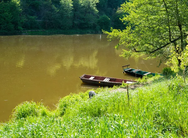 Zwei alte hölzerne Ruderboote mit üppigem Frühlingsgras am Ufer des Berounka-Flusses im Frühling mit Bäumen, Landschaft im goldenen Nachmittagslicht — Stockfoto
