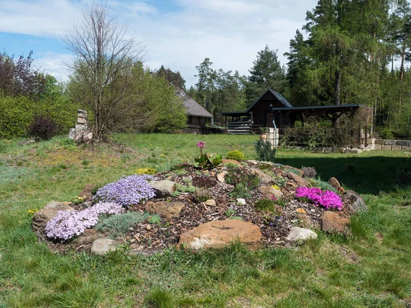 spring garden with beautiful rock garden in full bloom with pink Phlox, Armeria maritima, sea thrift, Bergenia or elephants ears, carnation and other colorful blooming flowers and gazebo or pergola