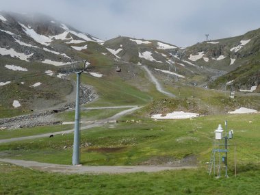 Avusturya, Tyrol 'daki Stubai Buzulu' nda Stubaier Gletscher teleferiği ve otlayan koyun ve ineklerle Mittelstation 'daki kar lekeli dağ yamaçlarına bakan manzara.