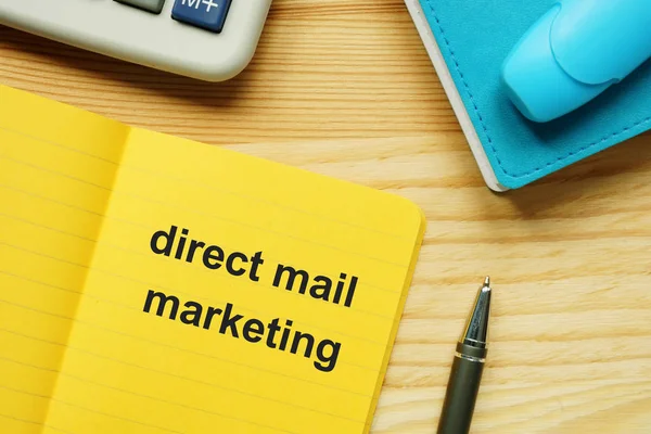 Text sign showing direct mail marketing. The text is written on a small colored paper. Keyboard, marker, wooden background are on the photo too.