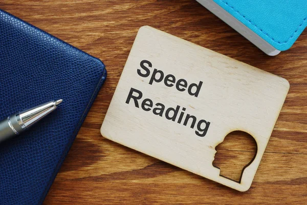 Writing note showing Speed Reading. The text is written on a small wooden board with the head silhouette. There are book, pen, colored papers on the photo.