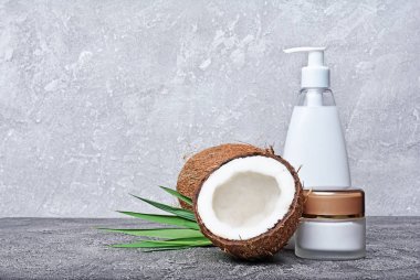 Boş beyaz mockup dağıtıcı şişe taze Hindistan cevizi ve gri beton zemin üzerine yeşil palmiye yaprağı ile kozmetik ürünleri