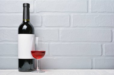 Boş etiket ve gri tuğla duvar arka plan üzerinde tatmak için cam ile kırmızı şarap şişesi