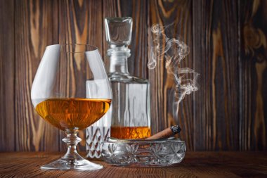 Ahşap doku arka plan üzerinde kül tablası içinde yasaktır puro ile güçlü alkollü içki konyak sniffer cam ve sürahi