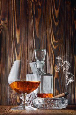 Ahşap doku arka plan üzerinde kül tablası içinde yasaktır puro ile güçlü alkollü içki konyak sniffer cam ve sürahi
