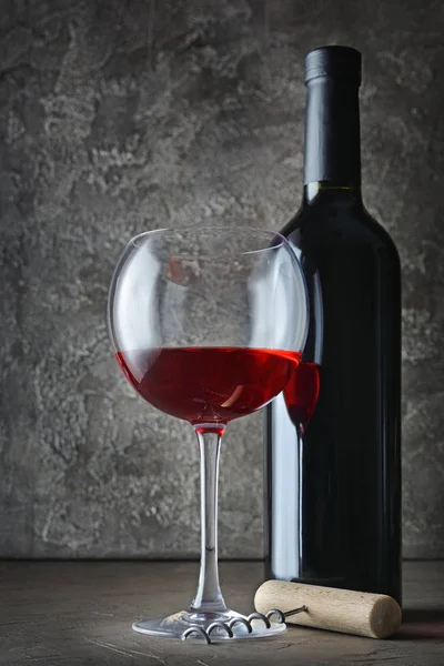 Kırmızı şarap şişesi ve tirbuşon gri beton zemin üzerine koyu mahzende ile tatmak için cam