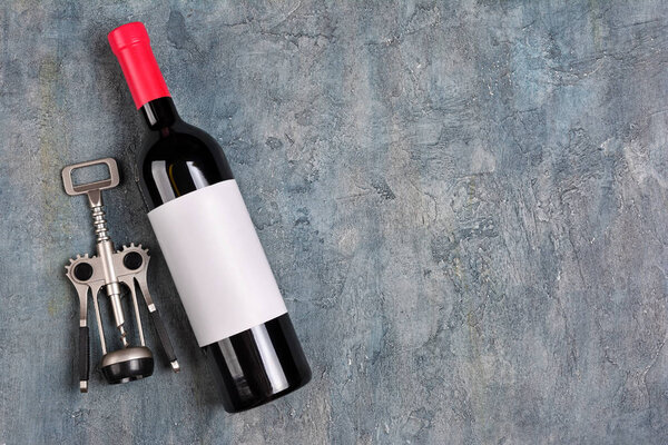 Плоская укладка лежащей красной бутылки вина с белой пустой этикеткой и штопор для дегустации на сером бетонном фоне

