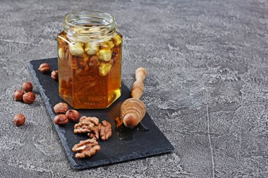 Sağlıklı doğal bal ile gri beton zemin üzerine bir kavanoza farklı fındık karışımı