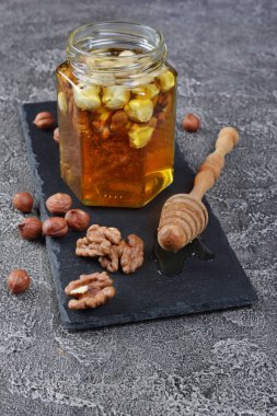 Sağlıklı doğal bal ile gri beton zemin üzerine bir kavanoza farklı fındık karışımı