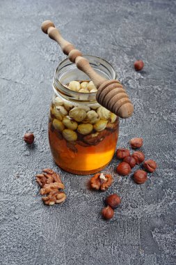 Sağlıklı doğal bal ile bir kavanoz ve gri beton zemin üzerine ahşap kepçe farklı fındık karışımı