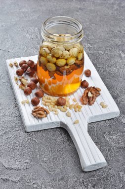 Sağlıklı doğal bal ile beyaz tahta ve gri beton zemin üzerinde bir kavanoza farklı fındık karışımı