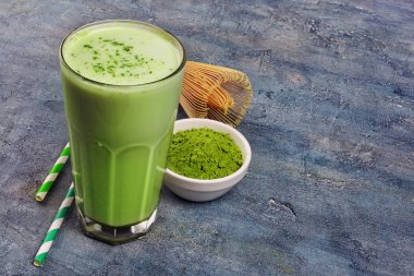 Organik yeşil matcha çay kahve cam ve bambu çırpma teli ve kokteyl saman kopya alanı mavi beton zemin üzerine beyaz kase toz