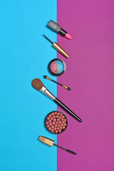 Top view on set of beauty products: decorative cosmetics as lip stick, mascara, eye shadow, blush, balls powder and makeup brushes on bright blue and purple background