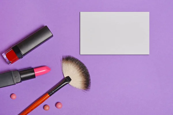 Top view on set of beauty products: decorative cosmetics as lip stick, nail polish, makeup brush and mock-up business card on bright purple background