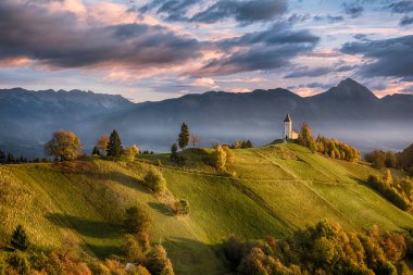 Kilise Jamnik Slovenya bulutlu gökyüzü ve dağlar arka plan mavi yeşil tepe üzerinde güzel gündoğumu peyzaj