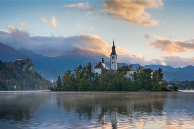 Ünlü dağ Gölü'nün güzel gündoğumu manzara mavi bulutlu gökyüzü ve dağlar arka plan üzerinde küçük yeşil adada Kilisesi ile Slovenya'da Bled