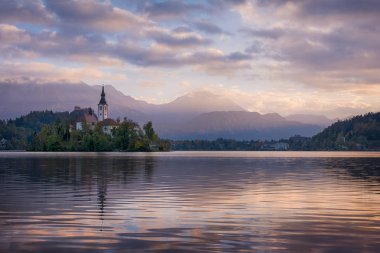Mor bulutlu gökyüzü ve dağlar zemin üzerine yeşil adada küçük kilise, ünlü lake Bled Slovenya güzel gündoğumu yatay