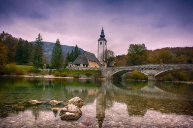 Göl Bohinj, Triglav Ulusal Parkı, Julian Alps Slovenya güzel gündoğumu manzara mavi bulutlu gökyüzü arka plan üzerinde kilise ve kemer köprü ile