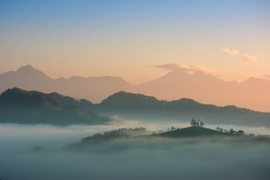 Saint Thomas Kilisesi Slovenya turuncu ve mavi gökyüzü ve Triglav dağ arka plan ile sabah sisin içinde tepenin üzerinde güzel gündoğumu peyzaj