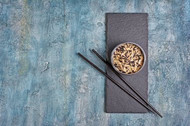 Kayrak tahta üzerinde ahşap Çin yemek çubukları ile siyah ve kahverengi pirinç pişmemiş ve mavi beton arka plan kopya alanı ile kase
