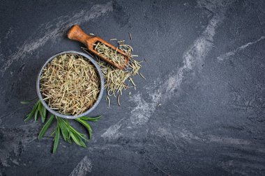 Üstten görünüm gri Seramik kase kuru baharat dolu yeşil yaprakları biberiye ve kopya alanı siyah mermer zemin üzerine ahşap kepçe ile el işi