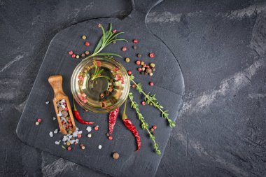 Aromatik veya aromalı zeytinyağı ile baharat ve otlar biber, biberiye ve kekik siyah ahşap tahta üzerinde cam kase ve mermer arka plan kopya alanı ile