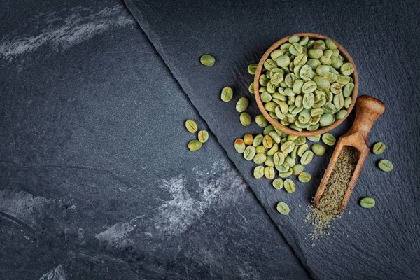 在木碗里的生绿色未烘焙咖啡的顶视图 在黑色石板板上的木勺和大理石背景上的磨碎的咖啡 并有复制空间 — 图库照片