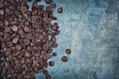 Top view of tasty dark chocolate drops or morsels scattered on blue concrete background with copy space clipart