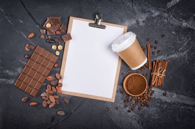 Mockup boş beyaz bir kağıt yaprağına ve tek kullanımlık eve servis kahve fincanı çikolata ve baharatlar ile üstten görünüm kopya alanı siyah mermer zemin üzerine