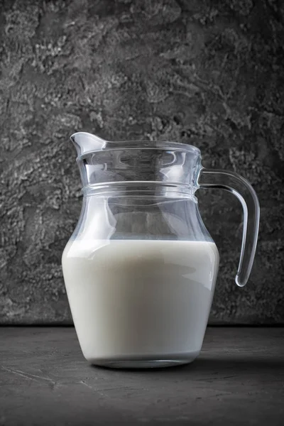 暗い灰色のコンクリート背景にガラスの水差しで健康的な自然な牛乳 — ストック写真