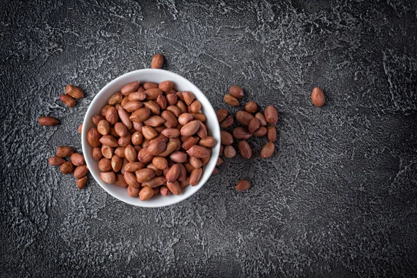 Koyu gri beton zemin üzerine beyaz kase doğal tüm fıstık üstten görünüm