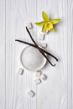Hafif ahşap arka plan üzerinde beyaz toz ve küp şeker vanilya çubukları ve çiçek ile üstten görünüm