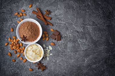 Kakao tozu ve badem dilimler halinde kopya alanı gri beton zemin üzerine şekerlemeler için madde olarak baharatlar ile beyaz kase üstten görünüm