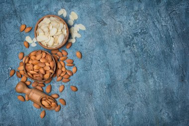 Ahşap kase ve kopya alanı mavi beton zemin üzerine şekerlemeler için madde olarak kepçe bütün fındık ve badem dilimleri üstten görünüm