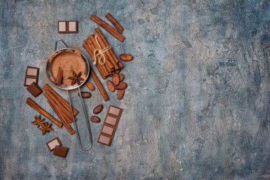 Kopya alanı mavi beton zemin üzerine şekerlemeler için çikolata, kakao çekirdekleri ve baharat olarak maddeler ile süzgeç içinde kakao tozu üstten görünüm