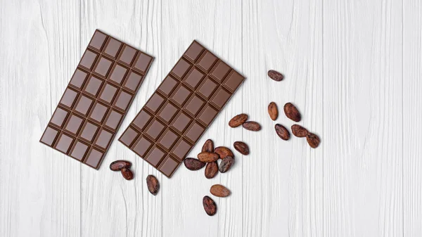 おいしいチョコレート スナックや木製の白い背景の上のお菓子の原料としてカカオ豆のトップ ビュー — ストック写真