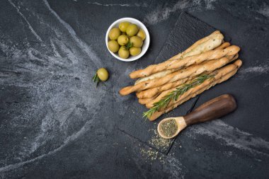 Geleneksel İtalyan meze grisini biberiye baharat ve yeşil zeytin ile üstten görünüm siyah arduvaz kurulu ve mermer arka plan kopya alanı ile