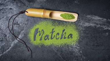 Siyah mermer zemin üzerine bambu kepçe ile organik yeşil matcha çay tozu gelen yazı üzerine üstten görünüm