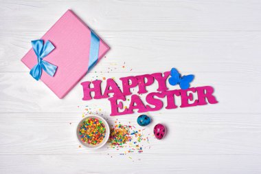 Pembe mavi saten yay ve parlak renkli boyalı bıldırcın yumurtası Beyaz ahşap zemin üzerinde mutlu Paskalya ve hediye kutusu metnin üzerinde üstten görünüm