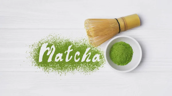 Top view on lettering from organic green matcha tea powder with bamboo chasen on white wooden background
