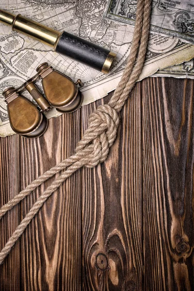 Top view on old map of the world on yellowed retro stained paper with vintage binocular, spyglass and knot of rope on wooden background with copy space