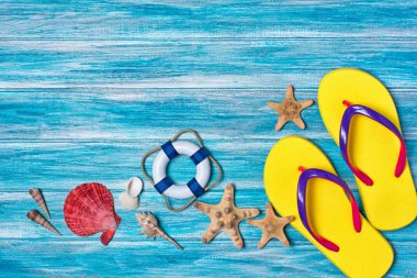 Üstten Görünüm parlak sarı kapak üzerinde deniz kabuklarını ve deniz yıldızı ile tatil zamanı kavram olarak kopya alanı ile mavi ahşap arka plan üzerinde floplar