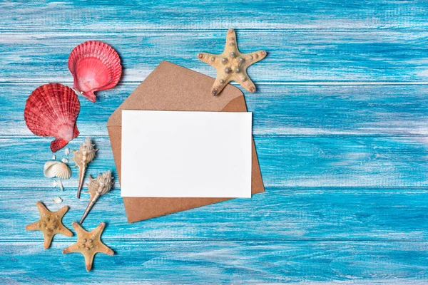 Deniz yıldızı ve mavi ahşap zemin üzerine kabukları ile kraft zarf üzerinde mock-up fotoğraf ya da yazı için beyaz kağıt kartı üzerinde Üstten Görünüm