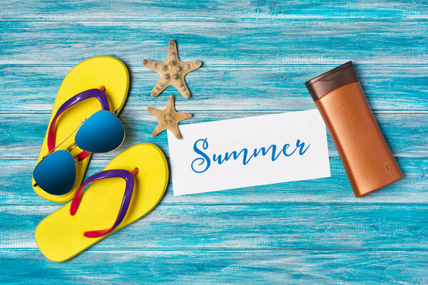 Top view on bright yellow flip flops with sunglasses and sunscreen as concept of vacation time on blue wooden background