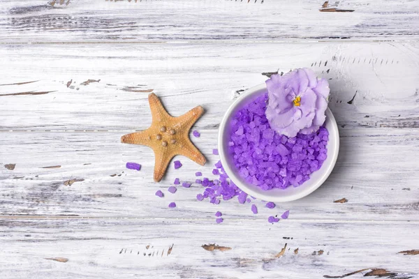 Smaksatt lila havssalt kristaller med violett blomma och sjöstjärna på vit — Stockfoto