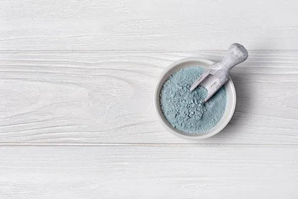 Polvo de arcilla cosmética azul en tazón con cuchara de madera sobre blanco — Foto de Stock