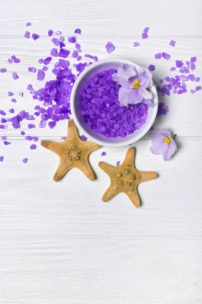 Fialové mořské soli s fialovou květinou a hvězdnými rybky na bílém — Stock fotografie