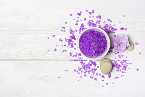 Aromatisierte lila Meersalzkristalle für den Wellnessbereich mit violetten Blüten und Steinen auf weißem Grund — Stockfoto